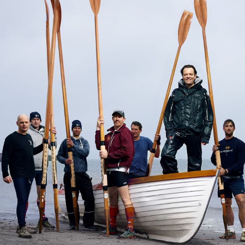 Mannen in sportieve outfit poseren bij en op een boot op het strand.